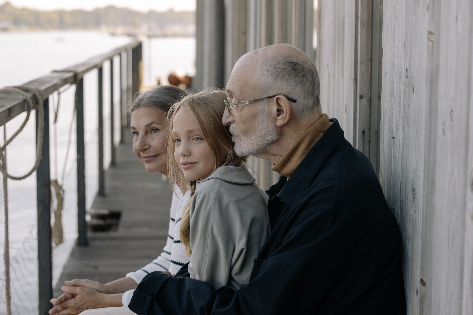 Three generations of a family sharing a quiet moment on a dock by the water.